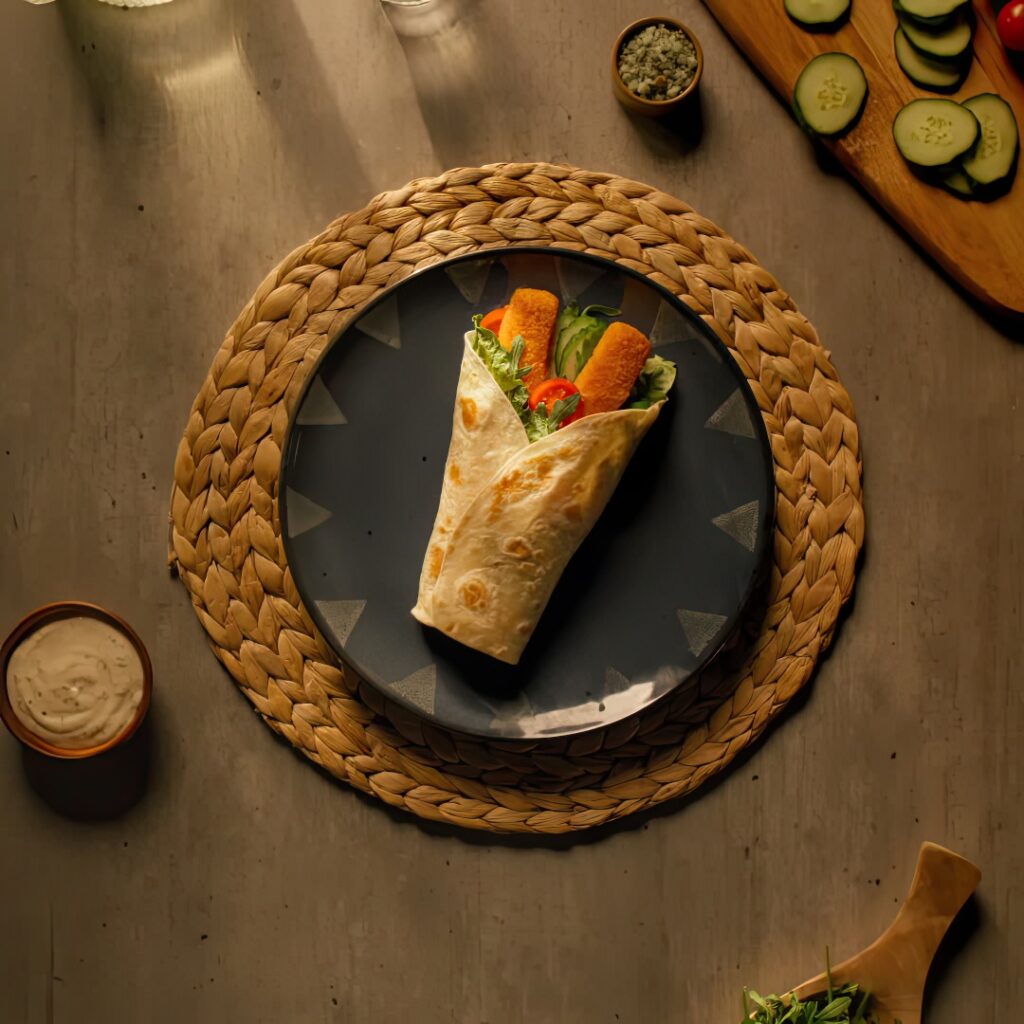 Zwinięta tortilla z złotymi paluszkami rybnymi, zieloną sałatą i czerwonym pomidorem na talerzu