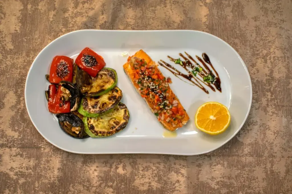 Grillowany filet z łososia FRoSTA, warzywa FRoSTA: papryka, cukinia i bakłażan, cytryna, glazura balsamiczna na białym talerzu.